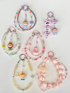 several bracelets and charms are arranged on a white surface, including one with a baby doll in the center