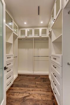 an empty walk - in closet with white cabinets and drawers on the wall, along with wood flooring