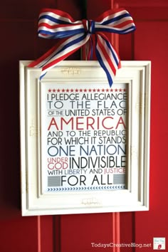 a patriotic frame hanging on the front door with a red, white and blue ribbon