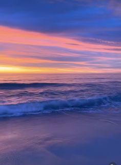 an ocean beach with waves coming in to the shore and colorful clouds above it at sunset