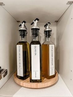 three bottles of liquid sitting on top of a wooden tray in a cabinet next to each other