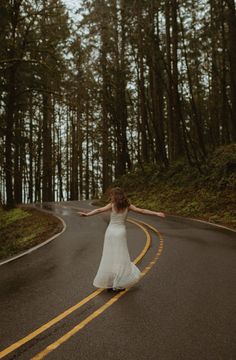 a woman in a white dress is walking down the road with her arms spread out