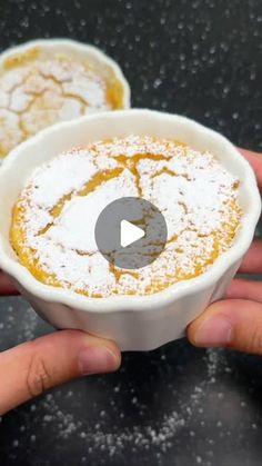 two hands holding small white bowls filled with powdered sugar and oranges on top of a black table