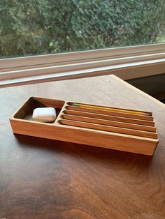 a wooden box with pencils and erasers in it sitting on a table next to a window