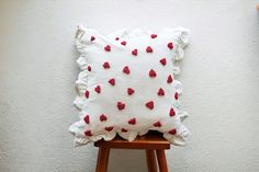 a white pillow with red hearts on it sitting on top of a wooden stool next to a wall