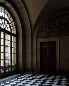 an empty room with black and white checkered flooring in front of large arched windows