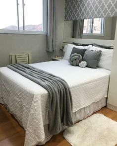 a white bed sitting in a bedroom next to a window with gray and white curtains