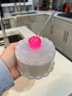 a hand holding a plastic container with a pink object in the lid and a straw sticking out of it