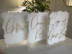 three clear acrylic signs sitting on top of a table next to a potted plant