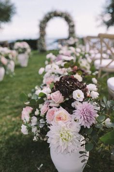 an outdoor ceremony with white and pink flowers in vases on the grass, surrounded by chairs