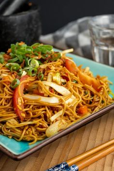 a blue plate topped with noodles and veggies next to two chopsticks