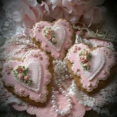 some heart shaped cookies with pink frosting and flowers on them are sitting on a lace doily