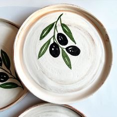 three white bowls with black olives painted on the sides and green leaves in the middle