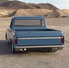 a blue pickup truck parked in the middle of an empty lot with mountains in the background