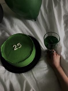 a green cake sitting on top of a bed next to a person's hand