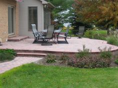 a patio with chairs and tables in front of a house next to a lawn area