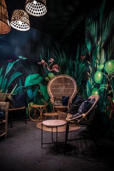 a room filled with lots of green plants and wicker furniture in front of a black wall