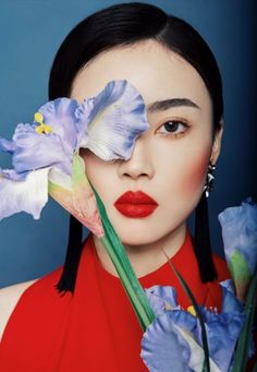 a woman with long black hair and red lipstick holding flowers in front of her face