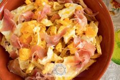 an orange bowl filled with eggs and ham on top of a floral tablecloth covered table