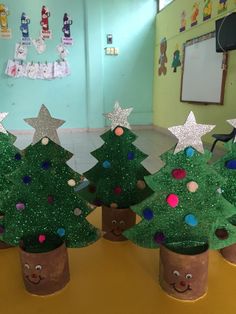 three potted christmas trees with faces and stars on them, sitting in a classroom