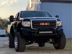 the front end of a black truck parked on top of a dirt road next to a building