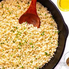 a pan filled with rice and a wooden spoon on top of it next to some seasonings