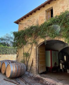 an old building with barrels in front of it and vines growing on the outside wall