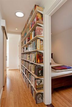 a book shelf filled with lots of books on top of a hard wood floor next to a bed