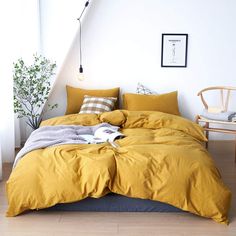 a bed with yellow comforter and pillows in a white room next to a chair