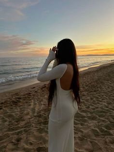 a woman standing on top of a sandy beach next to the ocean with her hands behind her head