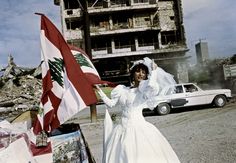 a woman in a wedding dress holding a flag next to a white car and building