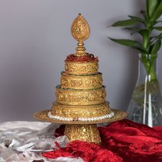 a three tiered cake sitting on top of a red table cloth next to a vase filled with flowers