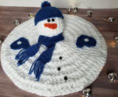 a crocheted snowman with blue hat and scarf on top of a wooden table