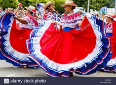 several women in colorful dresses and hats are dancing on the street while people watch from behind them