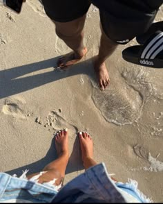 two people standing on the beach with their feet in the sand and one person wearing flip flops