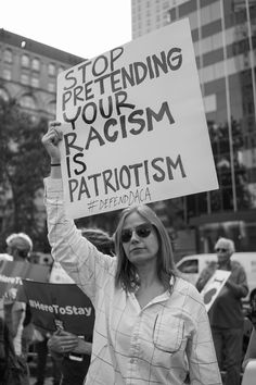 a woman holding up a sign that says stop pretending your racism is patriotism and defending democracy