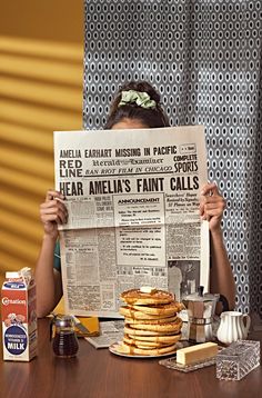 a woman sitting at a table holding up a newspaper with pancakes on top of it