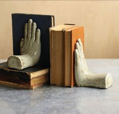 an open book with two hands sticking out of it next to a statue of a hand holding a book