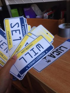 a person holding up four license plates on top of a wooden table with other items in the background