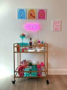 a bar cart with drinks on it in front of a neon sign that reads cocktails