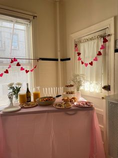 a table with food and drinks on it in front of two windows, decorated with paper hearts