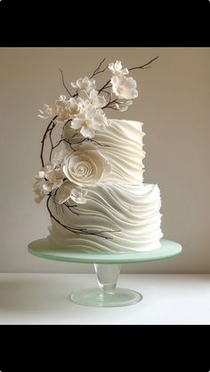 a white wedding cake with flowers on the top is sitting on a glass platter