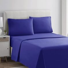 a bed with blue sheets and pillows in a white room next to a night stand