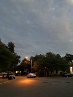 cars are parked on the side of the road at night with clouds in the sky