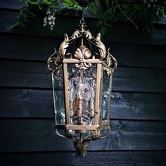 an old fashioned lantern hanging on the side of a building with candles in it and leaves