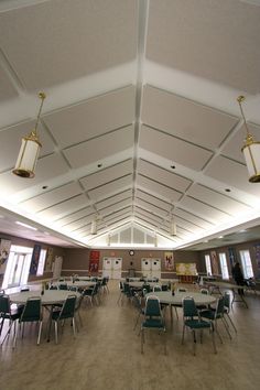 an empty room with tables and chairs in the center is lit by two hanging lights