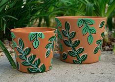 two planters with green leaves painted on them sitting in front of some grass and plants