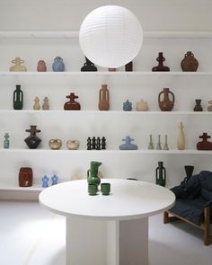 a white table topped with lots of bowls and vases next to shelves filled with bottles