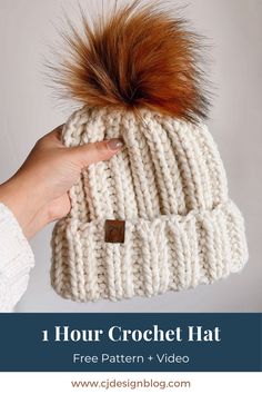 a hand holding a white knitted hat with brown pom - pom