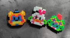 three pieces of bead art sitting on top of a gray cloth covered floor next to each other